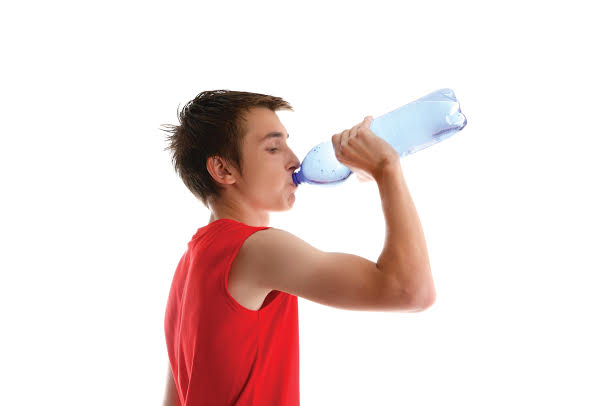 An active young boy teenager drinking bottled water after sport or exercise.  White background.